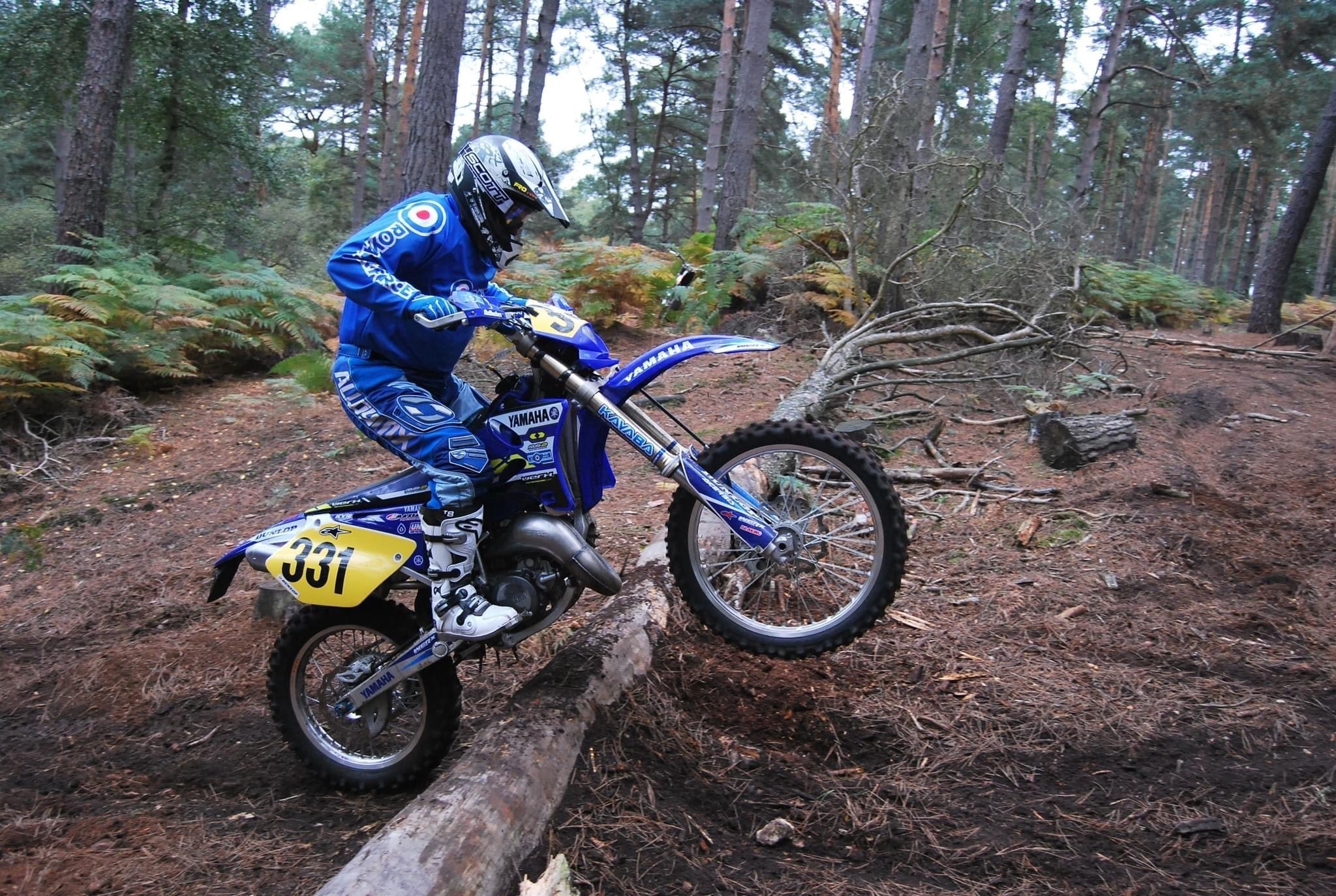 Enduro rider number 331 on a Yamaha clearing a fallen log on a forest trail