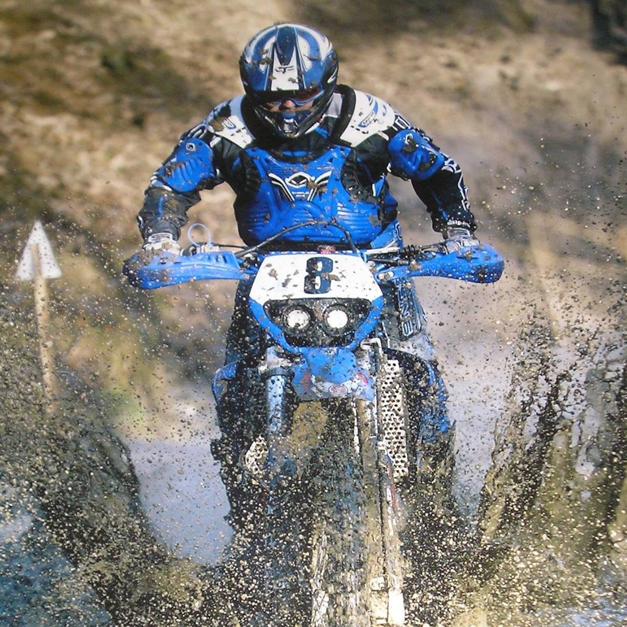 Enduro rider number 8 in blue kit blasting through a muddy water crossing